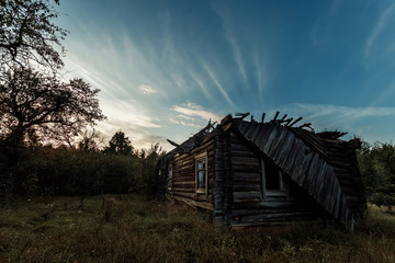 Creative background, an abandoned wooden house, a hut against a beautiful sunset. The concept of a magical background, fantasy, mysticism, devastation, old age.