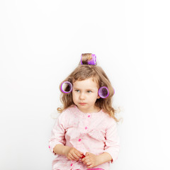 Beautiful little girl with curlers on her head looking at camera and having fun at home