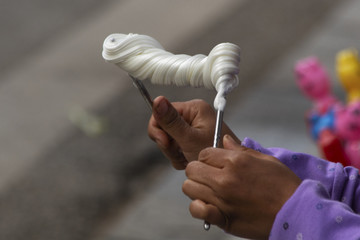 Close-up of woman twisting taffy-like confection on metal chopsticks