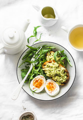Healthy breakfast or snack - boiled egg, arugula salad and avocado toast on a light background, top view