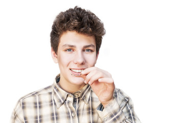 Teenager smiles on a white background and holds in his hand braces for leveling teeth. He is glad that he has already removed the braces