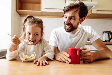 Family. Food. Parenthood. Dad and his little daughter are smiling while having a breakfast in the...
