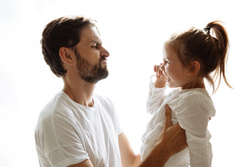 Parenthood. Family. Love. Dad is holding his little daughter in his arms and making faces. Girl is laughing. On white background