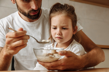 Family. Food. Parenthood. Dad is feeding his little daughter who is refusing to eat. In the kitchen...