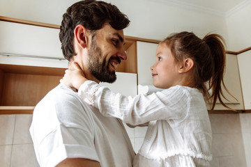 Fototapeta premium Parenthood. Family. Love. Dad is holding his little daughter in his arms. Both are looking at each other and smiling. In the kitchen at home