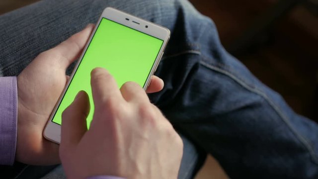 Man in the workplace using his smartphone with green screen, scrolling news, checking financial reports, tapping on screen. Hands top view.  4K Hands holding business finance smart phone CHROME KEY