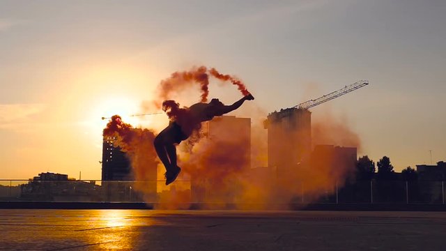 Young man holding colored smoke and doing backflip sommersault trick. Slowmotion.