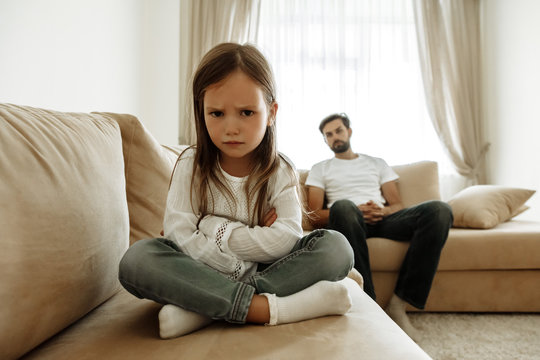 Childhood. Education. Problem. Offended little girl is looking at camera, her father in the background