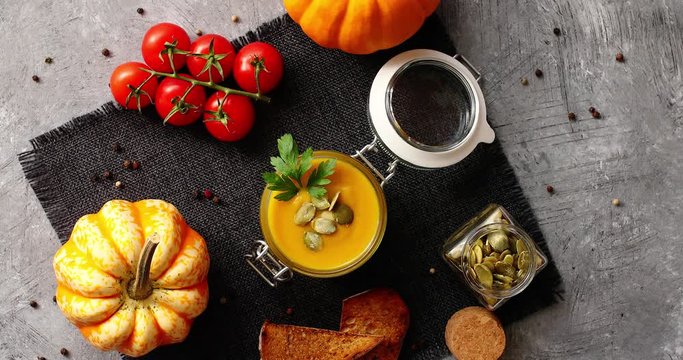 From above view of yellow pumpkin soup in glass jar surrounded by vegetables and pieces of bread placed on textile napkin