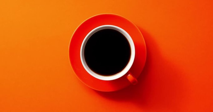 From above view of cup with black coffee placed on orange background