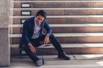 Businessman making mistake about financial business. Exhausted and tired worker surrendering to fatigue working with headache sit down on the stairs,