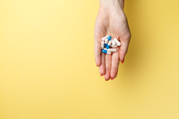 Colorful pills and tablets in the woman hand on yellow background. Top view. Flat lay. Copy space. Medicine concept