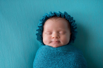 Smiling Newborn Baby Girl Wearing a Turquoise Blue Bonnet