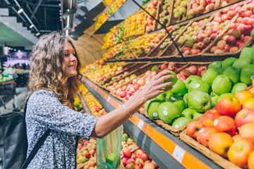 young adult woman choosing apples in grocery store
