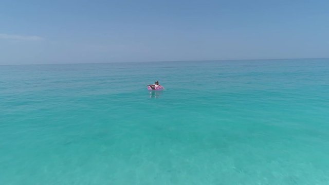 Aerial - Flyover adult female lying on donut floatie in the sea