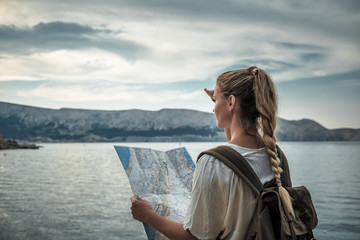 Hiker woman with map looking at sea bay while traveling