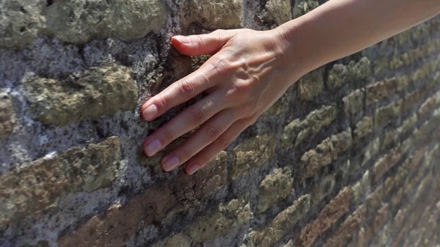 Woman sliding hand against old ancient red brick wall in slow motion. Female hand touching hard rough surface of stone bridge