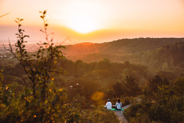 Obraz na płótnie Canvas couple of women sitting at the edge of the hill. do yoga exercises on sunrise