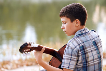 the boy plays an acoustic guitar, sits on the Bank of the river, autumn forest at sunset, beautiful nature and the reflection of trees in the water