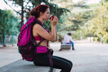 Young sportswoman sitting on bench and drinking coffee
