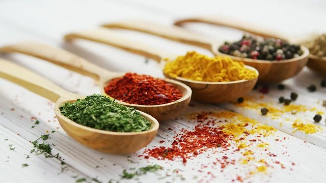 Row of wooden spoons filled with various multicolored spices and composed on wooden table