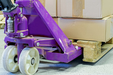 Purple hand pallet truck with cardboard boxes close up. 