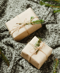 Gift boxes on a warm knitted gray plaid with Christmas tree branches. A cozy new year.