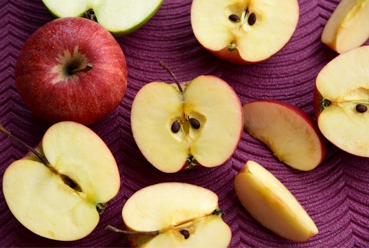 Many sliced red Gala apples on purple background.