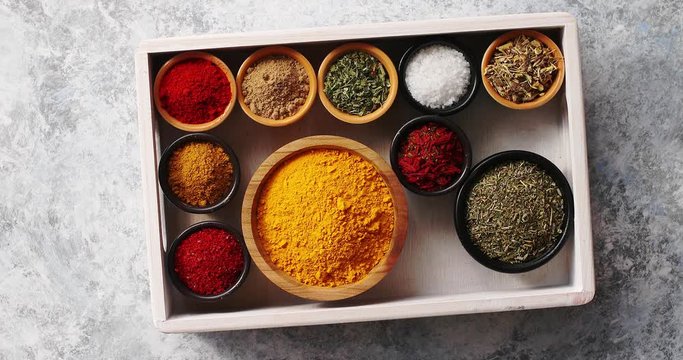 Top view of wooden tray filled with bowls full of ground colorful spices on marble table surface