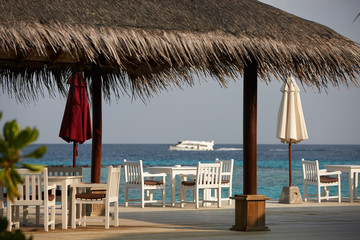 Fototapeta premium White empty table table and chairs at tropical resrraunt on open terrace in maldives. Blue ocean lagoon on background. No people.