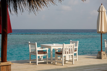 White empty table table and chairs at tropical resrraunt on open terrace in maldives. Blue ocean lagoon on background. No people.