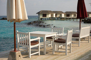 White empty table table and chairs at tropical resrraunt on open terrace in maldives. Blue ocean lagoon on background. No people.