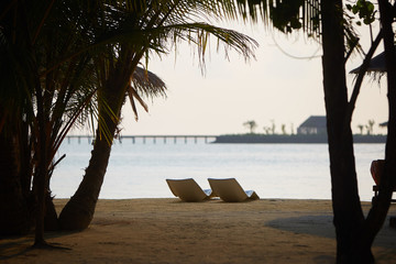 Two modern beach chairs on the beach. Indian ocean coastline on Maldives island. White sandy shore...