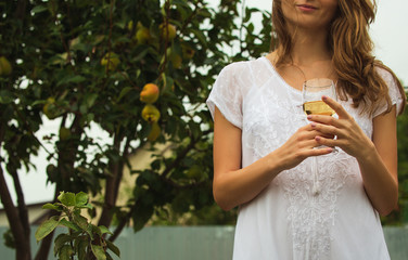 Beautiful Young Woman on a White Dress Holding  Glass of Pear Organic Cider on a Pear Tree Background. Garden Background. Harvest Concept