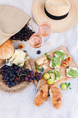 Romantic summer picnic with delicious food, two wineglasses, healthy fruits: avocado, grapes, figs. Straw hat, bag, sandwiches, croissants, cheese are on blanket. Breakfast in italian or french style