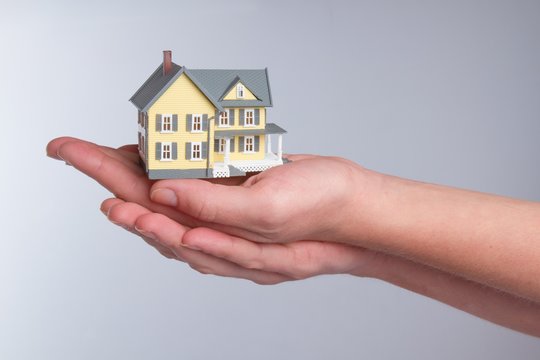 Cupped Hands Holding a Model of a House on Grey Background