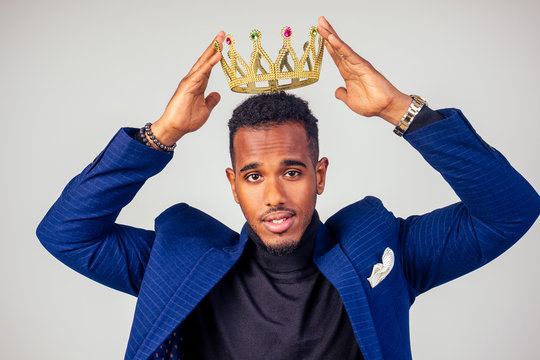 smart african american successful and rich businessman in a stylish suit and the golden crown on his head on white background in studio shot. the concept of well-deserved respect and luck