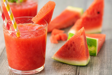 Watermelon smoothie in jars with fresh watermelon slices on gray wooden background