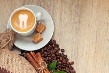Cup with espresso with coffee beans, burlap sack and cinnamon on light wooden background