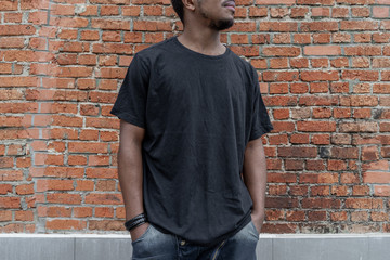 Close up of dark-skinned man in black blank T-shirt on bricked background.
