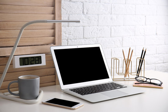 Modern workplace with laptop on table against brick wall. Mockup for design