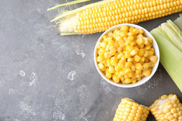 Bowl with corn kernels and ripe cobs on grey background, top view. Space for text