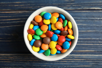 Bowl with colorful candies on wooden background, top view