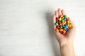Woman holding glazed candies on white wooden background, top view. Space for text