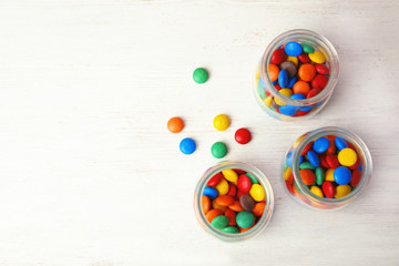 Jars with colorful candies on white wooden background, top view. Space for text