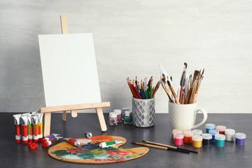 Naklejka premium Easel with various artist tools on table against light wall. Space for text