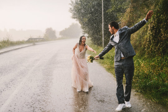 Totally wet just married couple walking on rain by drive road. Bride is train to catch her husband.