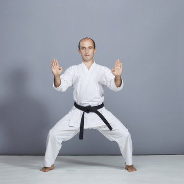 Young athlete with a black belt performs a formal karate exercise on a gray background