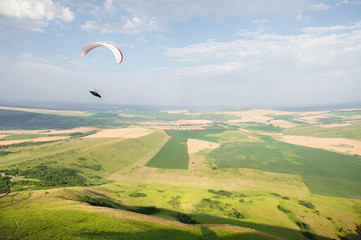 A white-orange paraglider flies over the mountainous terrain