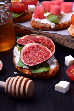 Assortment of bruschettas with figs, watermelon, cherry tomatoes, cheese and honey on a dark table